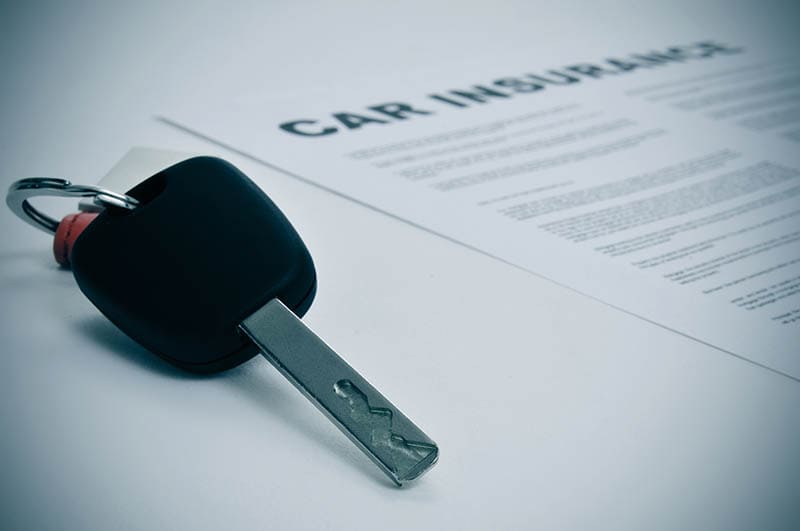 closeup of a car key and a car insurance policy