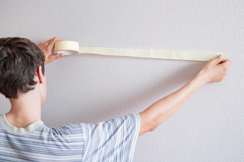 male worker using the masking tape to paint the wall