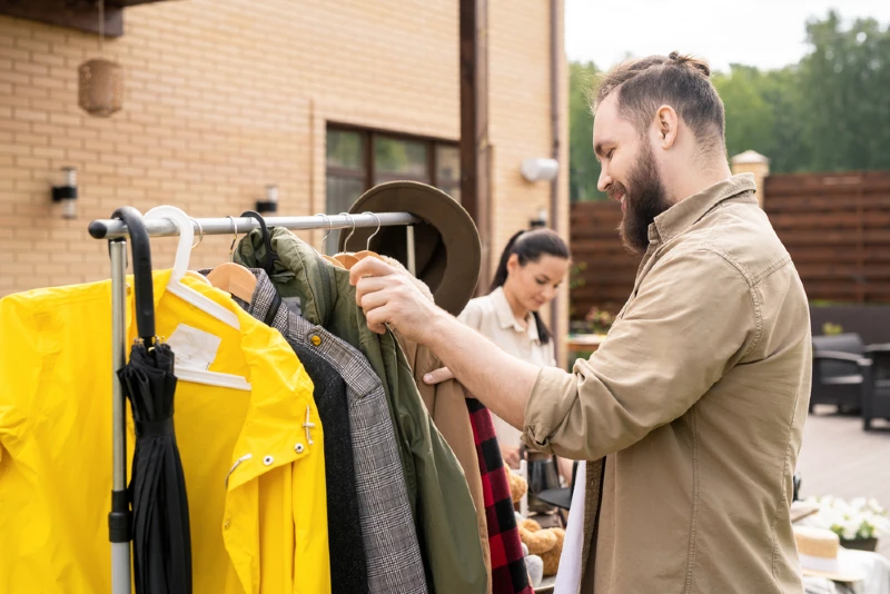man going through clothes hanging from a rack at a yard sale