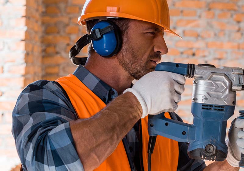 man using hammer drill near brick wall