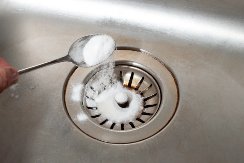 person pouring spoonful of baking soda into the drain