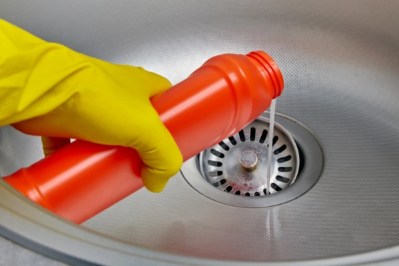 person with gloves pouring liquid cleaner into sink drain