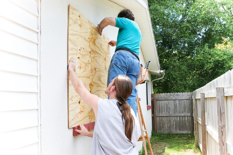 two people boarding up a house window in preparation for a hurricane or storm