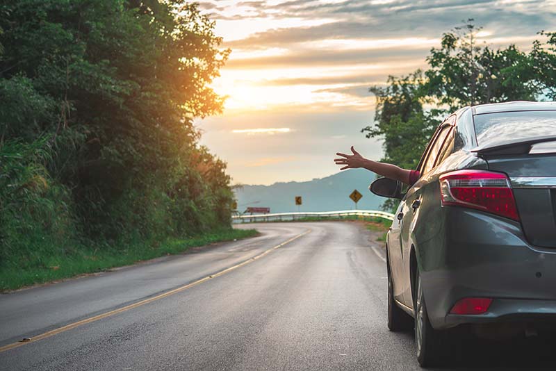 waving hand outside open window car with meadow and mountain