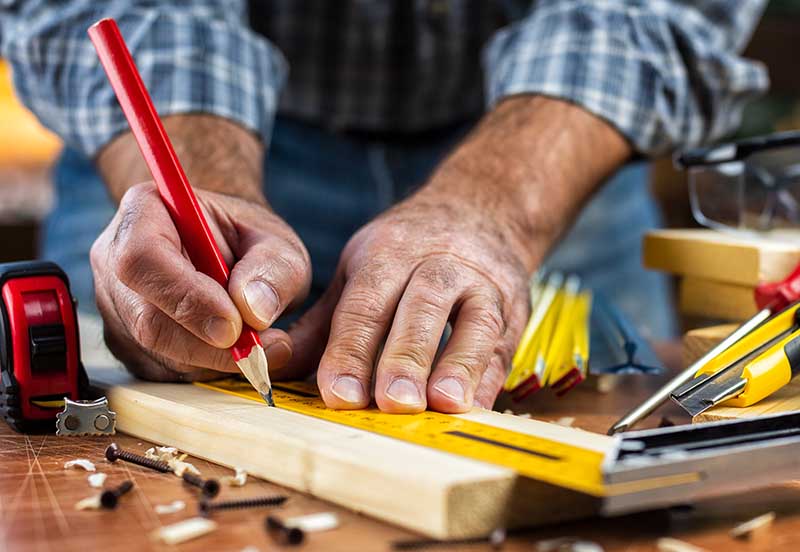 Adult carpenter craftsman with a pencil and the carpenter's square trace the cutting line on a wooden table