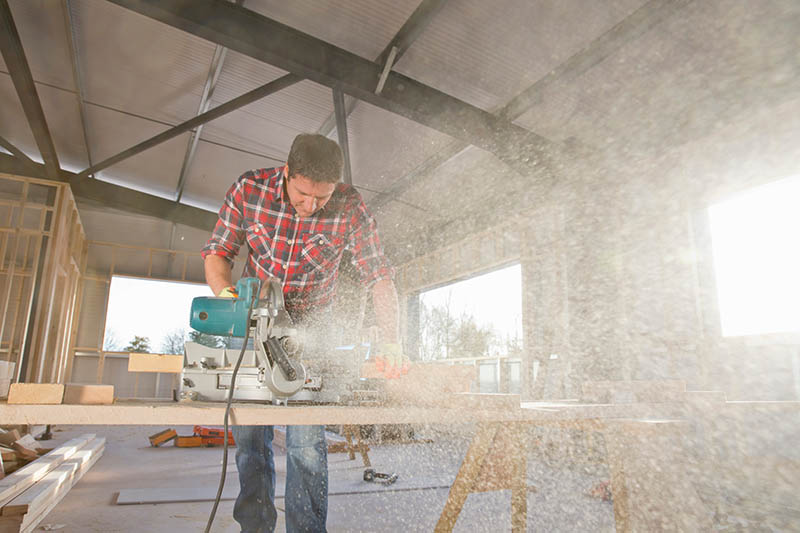 Carpenter cutting wood with circular power saw in building construction site interior