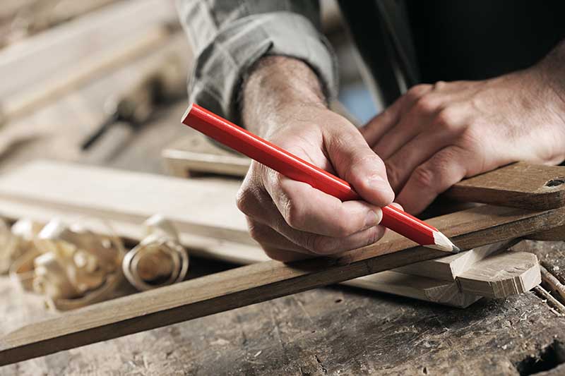 Close Up view of a carpenter using a straightedge to draw a line on a board