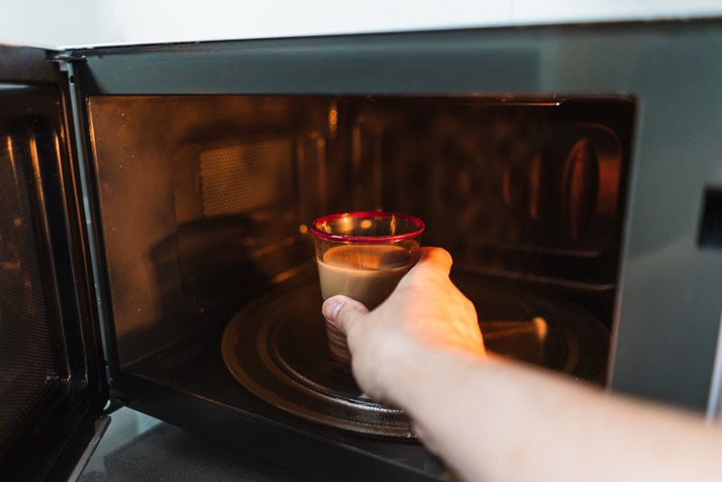 Hand putting a plastic cup with beverage inside a microwave oven