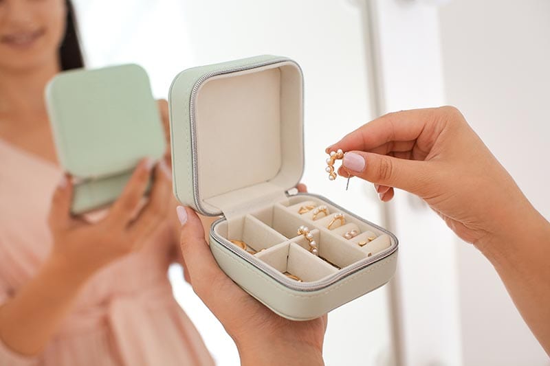 Young woman taking earring from jewelry box near mirror