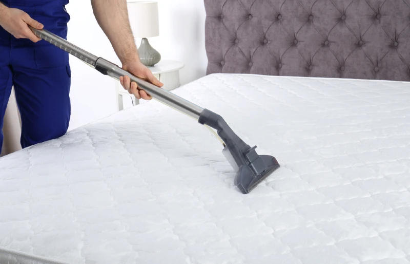 man disinfecting mattress using vacuum cleaner