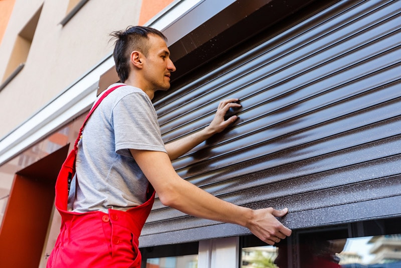 man installing roller shutter on window