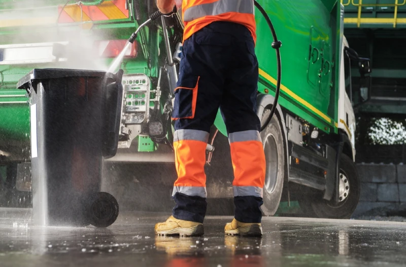man using a pressure washer to clean a trash bin