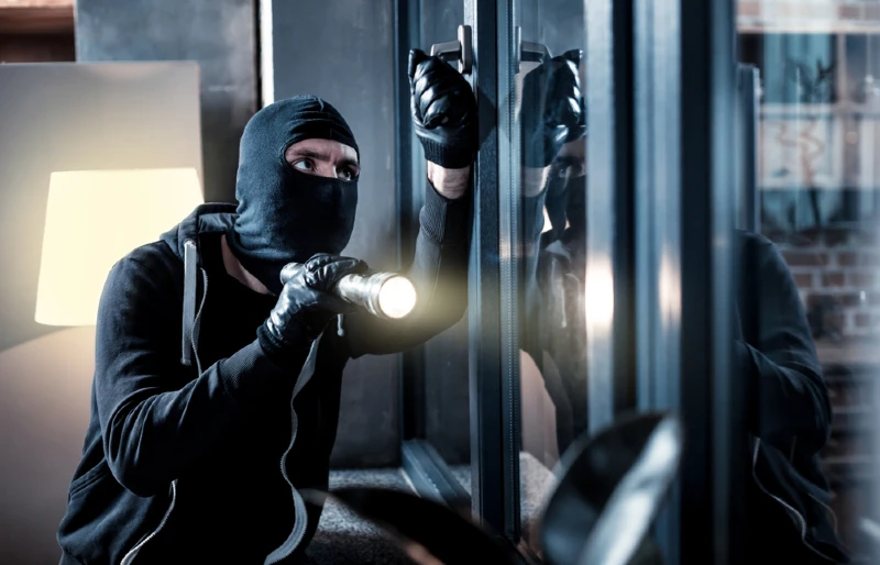 masked house burglar opening a window