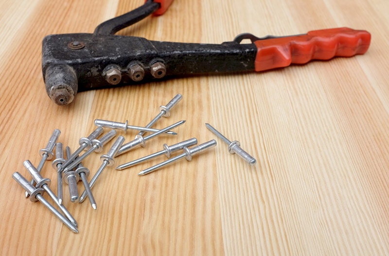 pop rivets and riveter tool on a wooden board