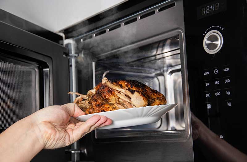 taking grilled chicken from modern microwave oven