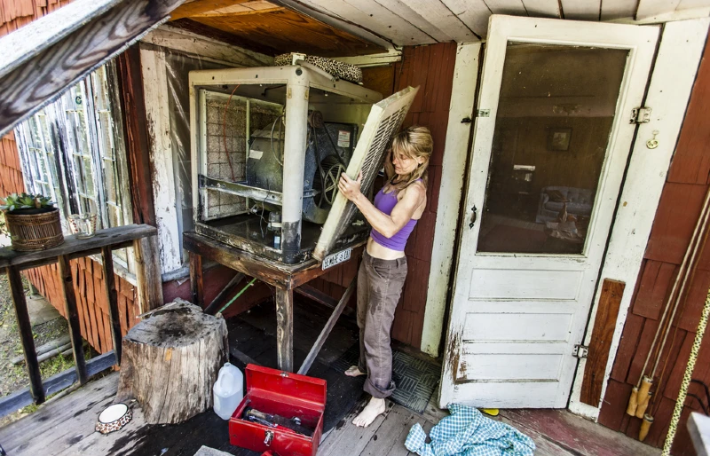 woman fixing a swamp cooler or evaporative cooler in a rustic cabin