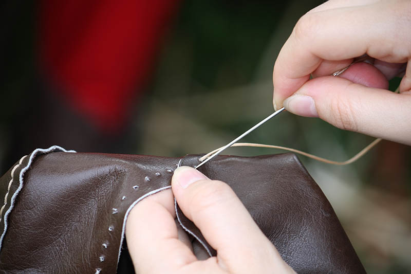 woman while sewing a dress in leather with needle and thread