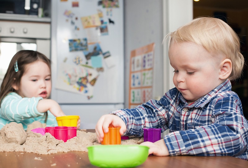 A cute little blond boy and a little girl play with kinetic sand at home