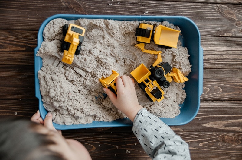 Child playing with kinetic sand and toy construction machinery