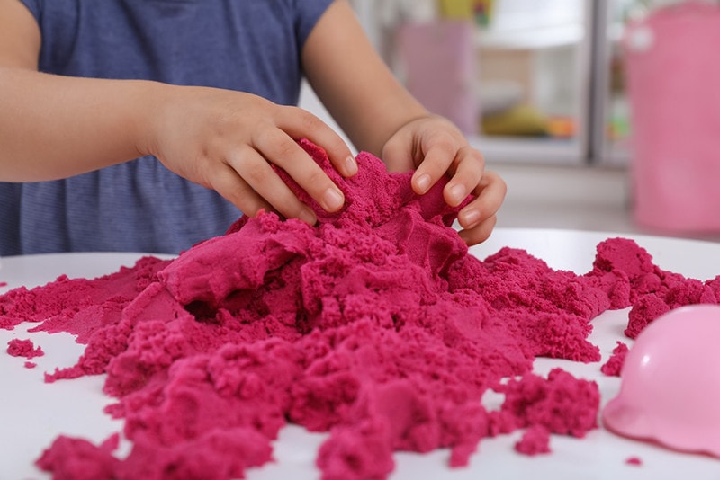 Little girl playing with bright kinetic sand at table