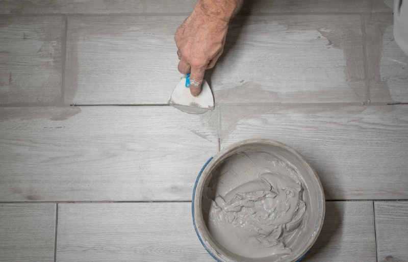 worker applying grout between tiles with a rubber trowel