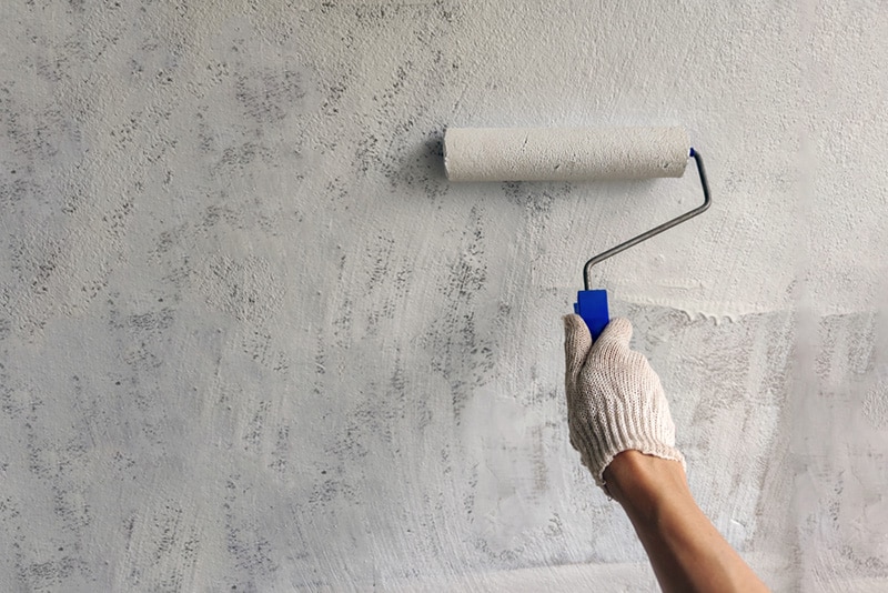 A girl paints a wall with white paint hand with roller for painting close up with copy space