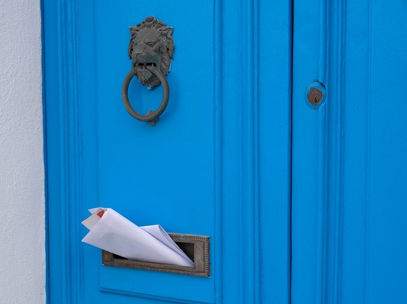 Blue vintage door with a knocker in the shape of a lion, mailbox slot in the door with advertising newspapers