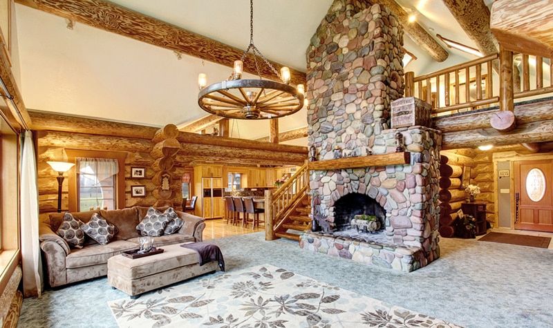 Bright Living room interior in American log cabin house. Rustic chandelier, stone fireplace and high ceiling with wooden beams make room gorgeous