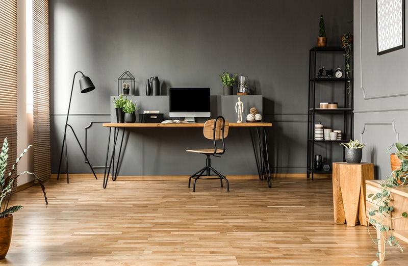 Chair at wooden table with computer monitor and plants in grey spacious home office interior