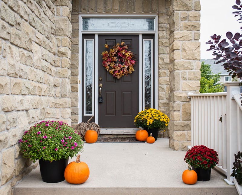 Front door of home decorated for fall with flowers and pumpkins