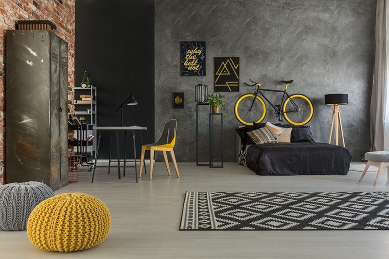 Grey apartment with bed, desk, chair, brick wall, yellow details
