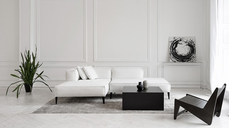 Modern white designer sofa on legs with cushions on grey carpet in middle of minimalistic living room