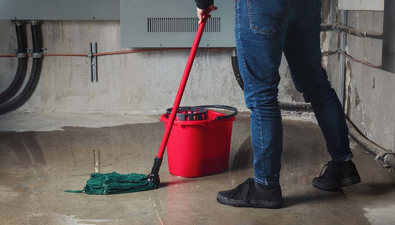 Woman mopping flood from water leaks in basement or electrical room