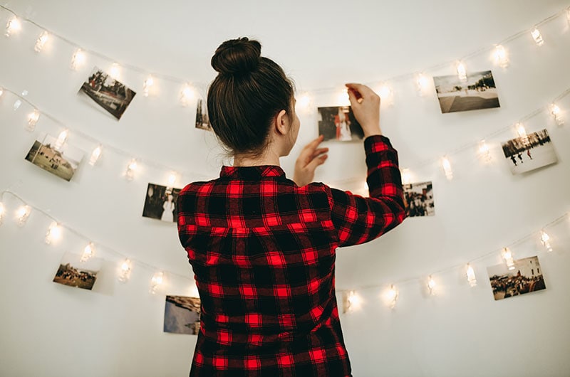 Young beautiful woman hangs a photos on a garland with light on the wall