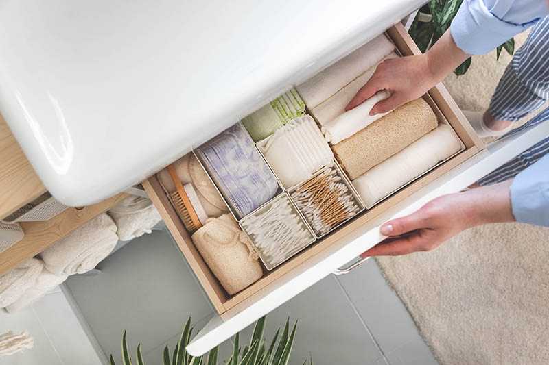 Top view of woman hands neatly organizing bathroom amenities and toiletries in drawer or cupboard in bathroom