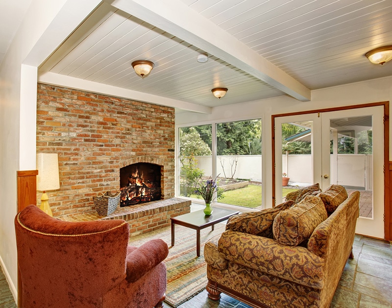 View of the living room area with white wooden ceiling and brick wall with fireplace