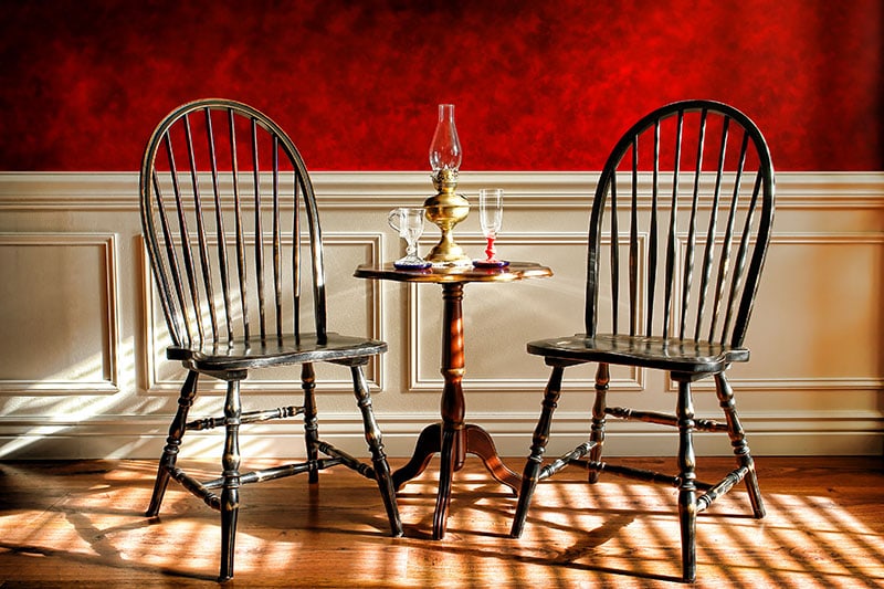 Antique black Windsor style chairs and mahogany table with glasses and oil lamp