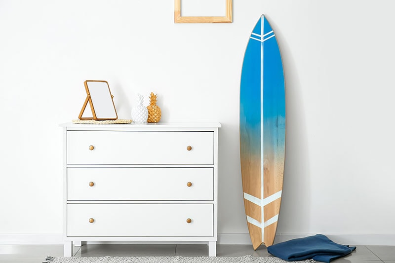 Interior of modern stylish room with chest of drawers and surfboard