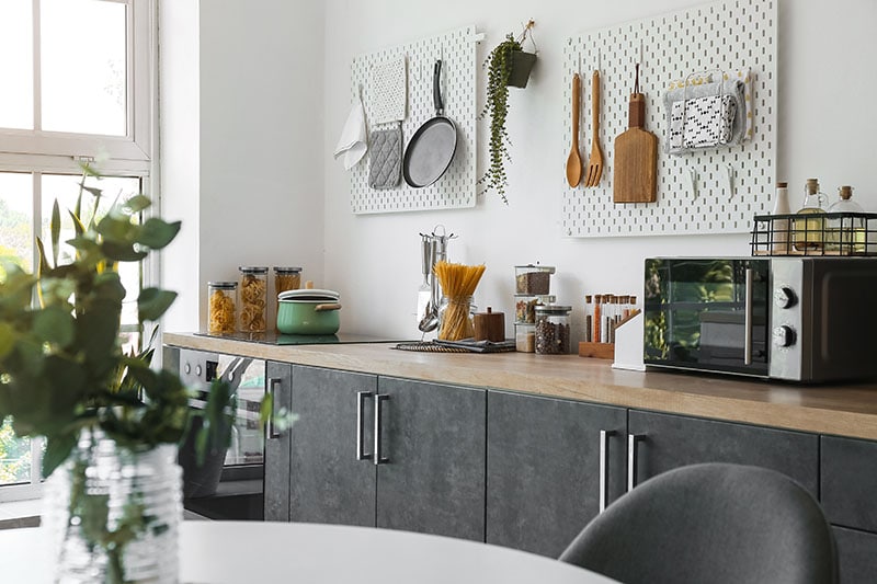 Stylish counters with utensils and pegboards on light wall in kitchen