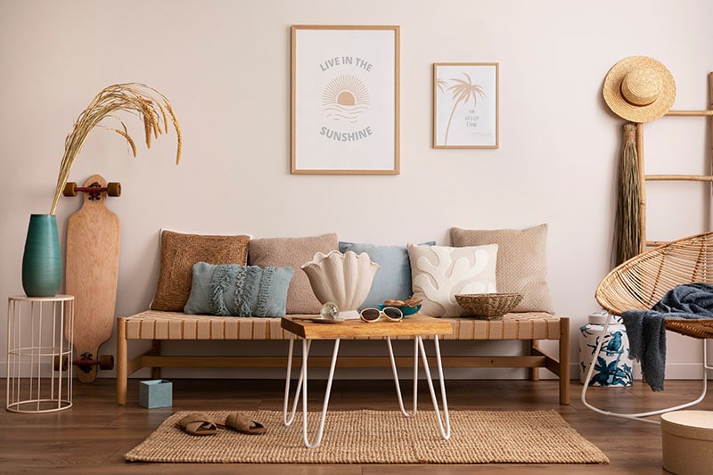 Sunny and bright space of living room with stylish sofa, pillows, coffee table, mock up poster frames, decorations, furnitures and personal accessories.